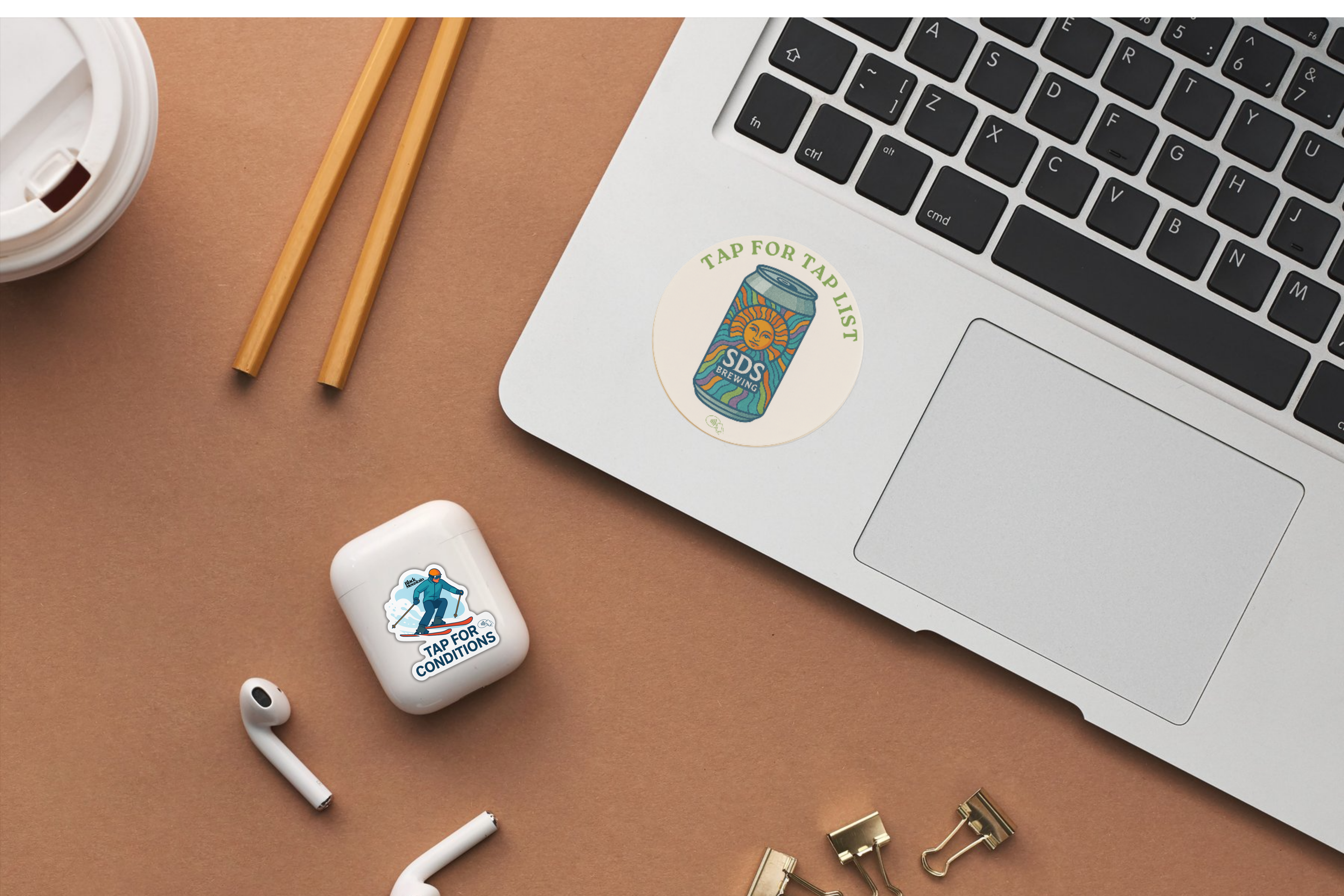 Laptop with a NFC sticker, airPod case with a NFC Sticker, and office supplies on a brown surface